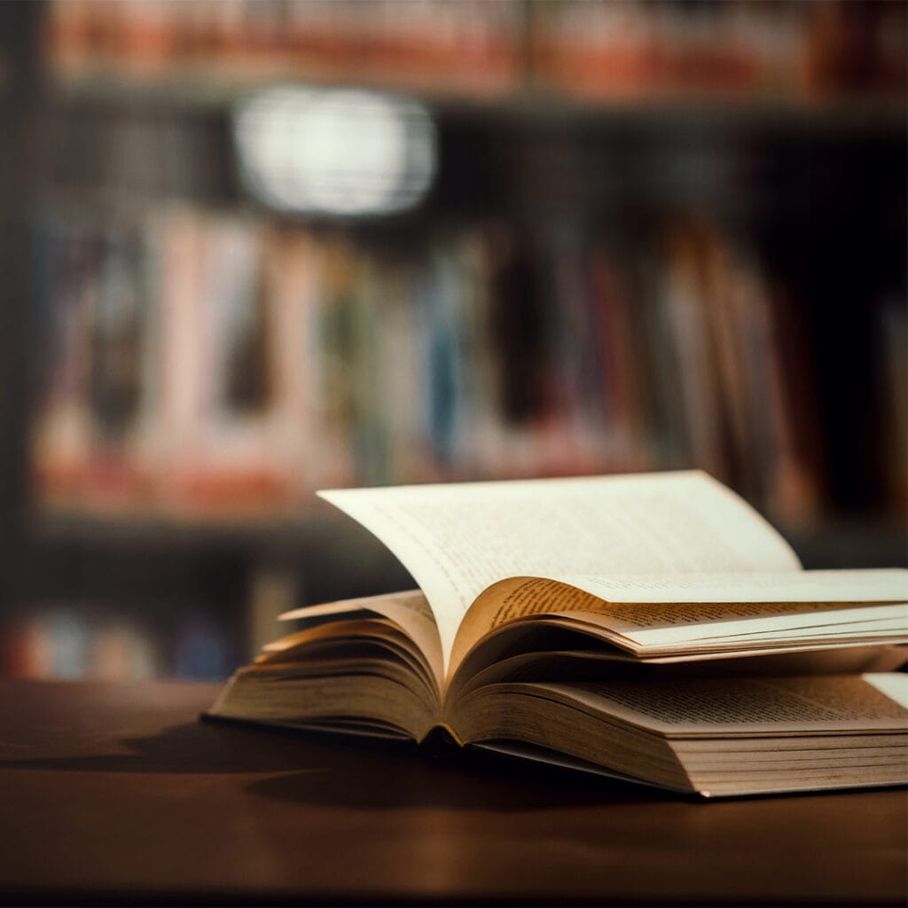 Livro aberto em cima de uma mesa com estantes desfocadas ao fundo, representando o ambiente acolhedor das livrarias.
