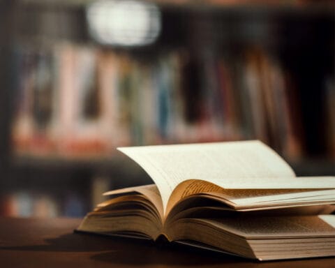 Livro aberto em cima de uma mesa com estantes desfocadas ao fundo, representando o ambiente acolhedor das livrarias.