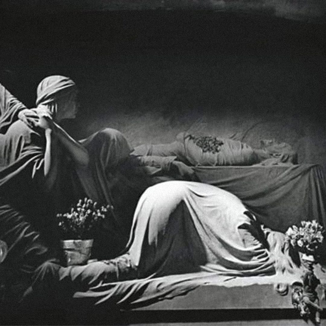 Escultura monocromática evocativa com figuras cobertas por véus fúnebres — estética associada ao imaginário visual de Joy Division.