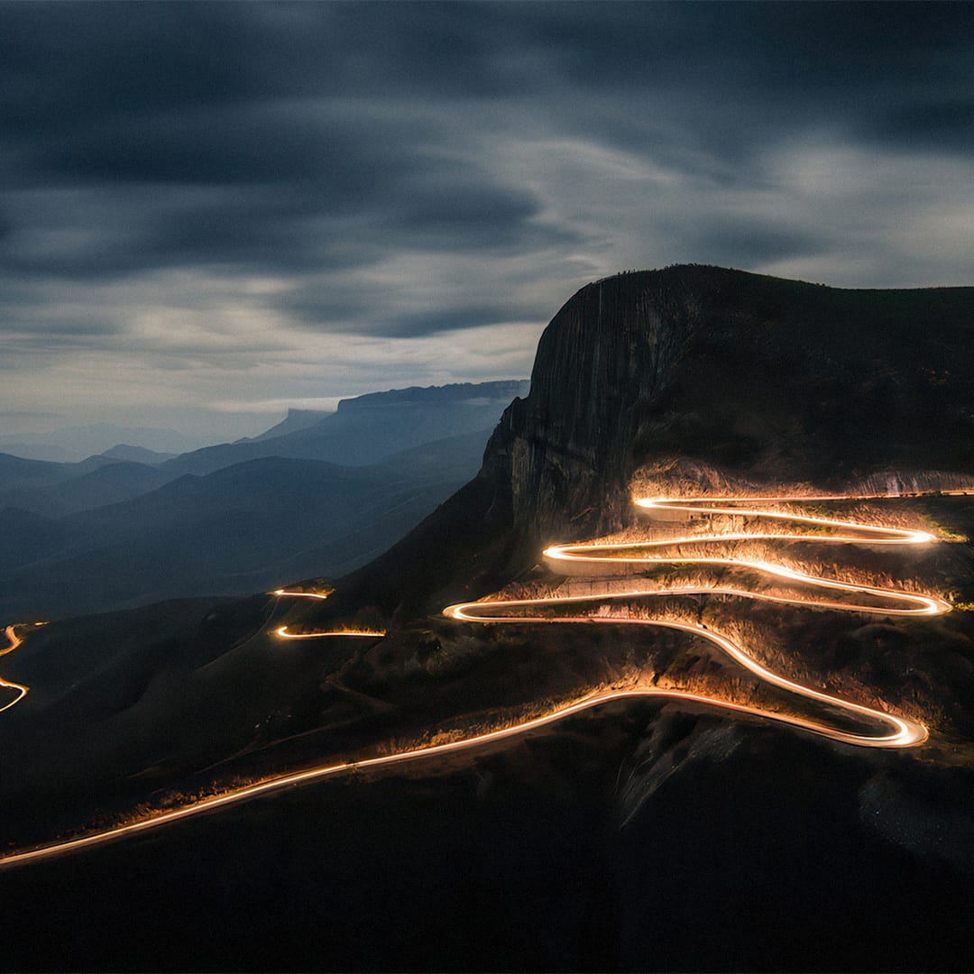 Estrada iluminada a serpentear pela montanha da Serra da Leba ao anoitecer.