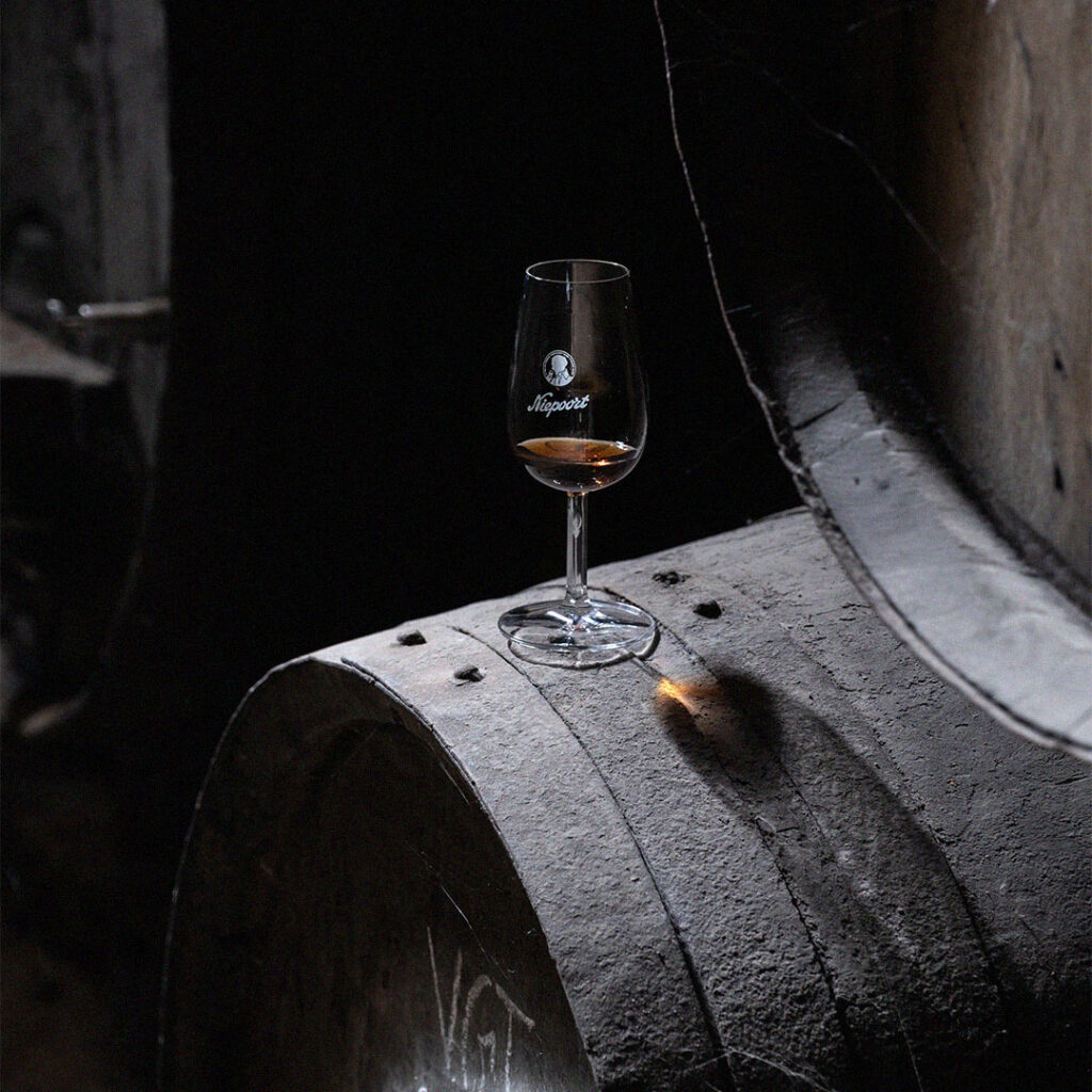Copo de vinho tinto sobre barrica de madeira numa cave de envelhecimento.
