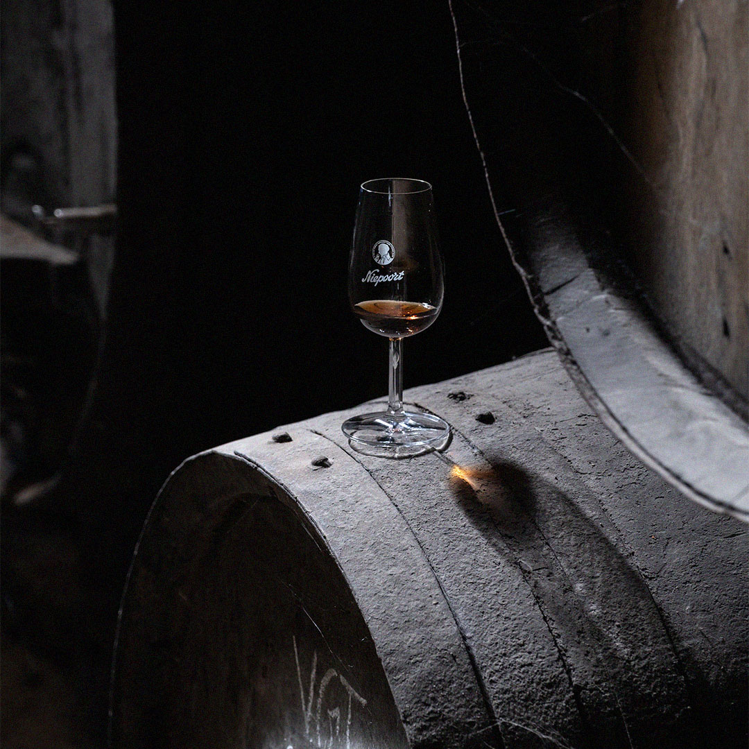 Copo de vinho tinto sobre barrica de madeira numa cave de envelhecimento.