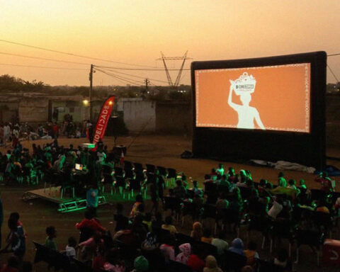 Sessão de cinema ao ar livre do Cine Zunga com público em Luanda ao entardecer.