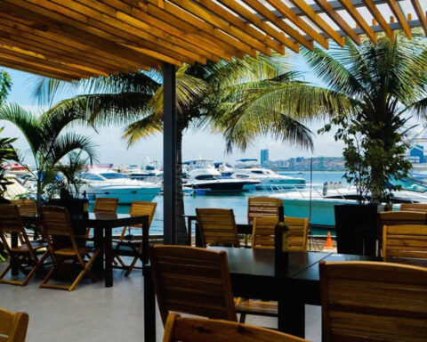 Esplanada de restaurante na Marina de Luanda com vista para iates, palmeiras e a baía.