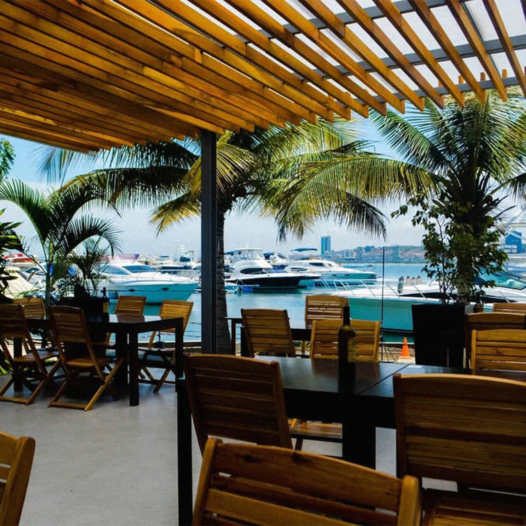 Esplanada de restaurante na Marina de Luanda com vista para iates, palmeiras e a baía.